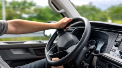 Close-up of a drivers hand on the top of the steering wheel during a drive. Interior scene captures a relaxed and realistic driving moment.